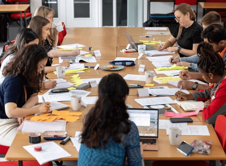diverse group of people meeting around a table, writing and collaborating, representing community project planning and engagement.
