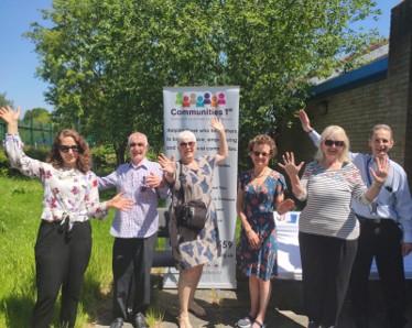 Photograph of people outide with their hands up next to a Communities 1st banner