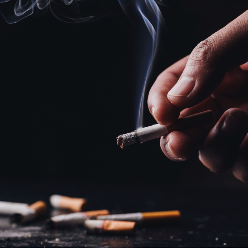A lit cigarette with a pile of a bunch more.