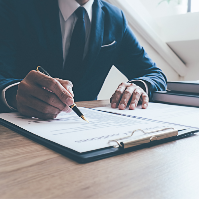 Somebody in a suit writing on a piece of paper attached to a clipboard.
