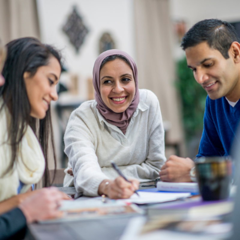 Four people sitting at a table, working together and smiling